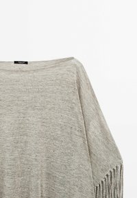 Grauer gestrickter Poncho mit weitem Halsausschnitt und strukturiertem Stoff. Besitzt lange Fransen am Saum für zusätzliche Details.