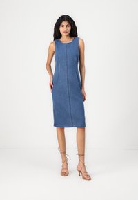 Džinsinė midi suknelė su prigludusia siluetu, apvaliu iškirpimu ir matomomis siuvimo detalėmis. Sujungta su diržinėmis šviesiai rudos spalvos aukštakulnėmis bateliais.