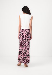 Vit ärmlös topp kombinerad med en lång rosa kjol med svart leopardmönster, slät textur och en subtil lyster.