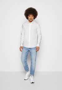 Camicia bianca button-up, jeans azzurri chiari e sneakers bianche. Tessuto della camicia liscio, colletto standard e jeans a taglio dritto.
