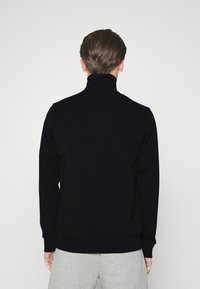 Svart polotröja i mjukt tyg, med en åtsittande design, ribbstickade ärmslut och hög krage för extra värme.