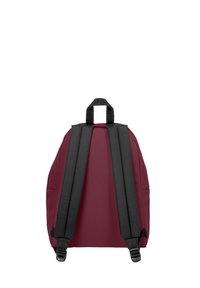 Mochila marrón con correas ajustables negras, de forma redondeada y con un asa superior. Textura suave y diseño minimalista sin bolsillos o acentos visibles.