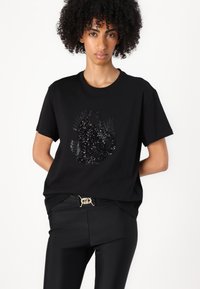 T-shirt in cotone nero con un design di un gatto decorato con paillettes, colletto rotondo, maniche corte, abbinato a pantaloni neri con una cintura dorata.