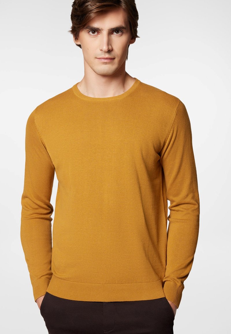 Musztardowy sweter z okrągłym dekoltem, z długimi rękawami oraz ściągaczami u dołu i na rękawach, wykonany z miękkiej, teksturowanej dzianiny.