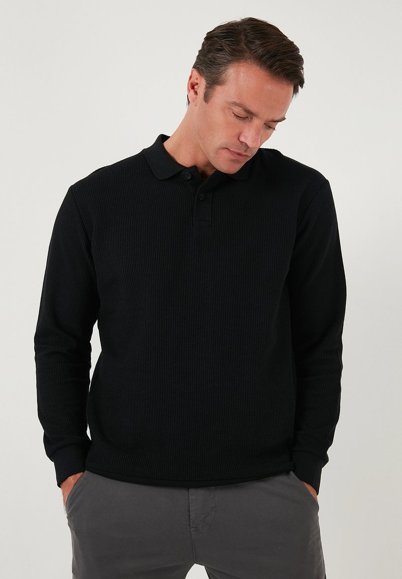 Camisa polo de manga larga negra, fabricada en tejido acanalado, con tapeta de tres botones y puños acanalados, que presenta un dobladillo recto.