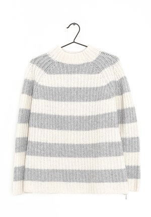 Weißer und grauer dicker Strickpullover mit horizontalen Streifen, der an einem schwarzen Metallbügel vor weißem Hintergrund hängt.