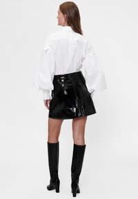 Bela majica z dolgimi rokavi in voluminoznimi rokavi, kombinirana z visokim črnim minikrupnim usnjenim krilom in črnimi škornji do kolen.