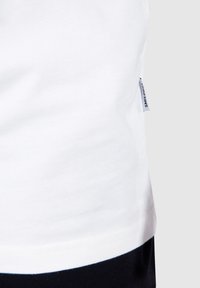White cotton t-shirt with navy blue hem. Smooth texture, short sleeves, featuring a small brand label on the left side near the bottom.