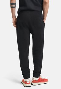 Sorte joggebukser med tapered ben, ribbede manchetter og en baglomme. Bærende med røde og cremefarvede sneakers med teksturerede detaljer.