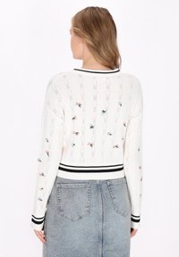 Pulover alb tricotat cu dungi verticale și broderie florală. Are un guler și manșete ribbrate alb-negru. Se asortează cu o fustă din denim.