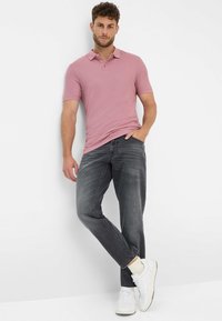 Polo a maniche corte rosa chiaro, abbinato a jeans grigio scuro. Sneakers bianche con dettagli crema completano il look. Design semplice e moderno.