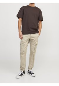 Mörkbrun t-shirt med kort ärm som kombineras med ljusbeiga cargobyxor med flera fickor, bärs tillsammans med svarta sneakers och vita snören.