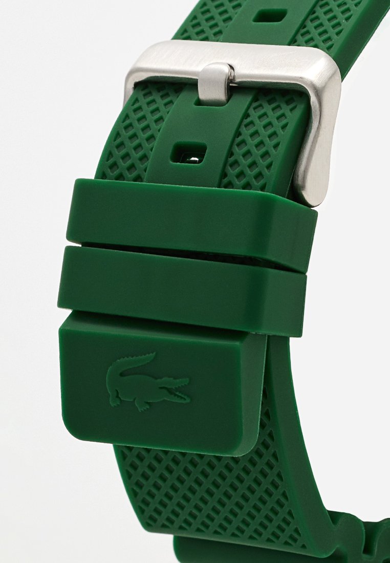 Correa de reloj de silicona verde con superficie texturizada, hebilla de metal plateado y detalle del logo de cocodrilo en relieve.
