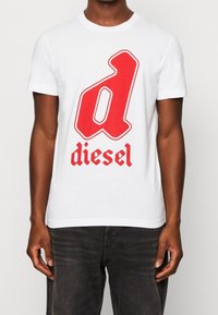 Vit bomull t-shirt med ett stort rött stiliserat "d" och ordet "diesel" i röd gotisk stil, korta ärmar och rund halsringning.