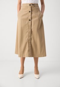 Jupe midi kaki avec un devant boutonné, des poches poitrine et une taille élastique. Tissu lisse et léger de couleur neutre.