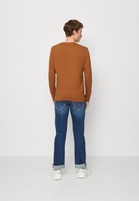 Brun langermet skjorte, avslappet passform, paret med mørkeblå jeans, oppbrettet i kanten, og hvite sneakers. Enkel, uformell design.