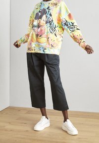 Sweatshirt multicolore avec un grand graphique de Mickey Mouse, présentant des motifs vibrants. Associé à un pantalon large noir et des baskets blanches.