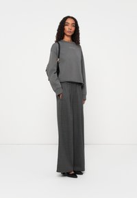 Grijze cropped sweatshirt met een ronde halslijn, gecombineerd met brede geruite broeken in grijstinten. Zwarte schoenen en een kleine zwarte tas.