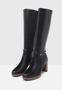 Bottes noires en cuir montantes avec une finition texturée, dotées d'une fermeture éclair sur le côté, d'un talon en bois et d'accents de sangle décoratifs.