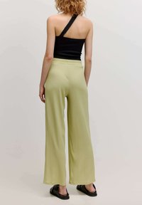 Helle grüne, weit geschnittene Hose mit strukturiertem Finish, elastischem Bund, kombiniert mit einem schwarzen, gerippten Top mit einem Schulterträger und schwarzen Sandalen.
