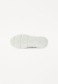 Suela de una zapatilla blanca que presenta una superficie de goma texturizada, patrones de banda de rodadura pronunciados y un diseño geométrico para una mayor tracción.