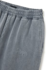 Grijze sweatpants gemaakt van zacht materiaal, met een elastische tailleband, zijzakken en geborduurde "Utopia"-tekst nabij de zoom.