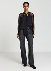 Blusa nera con maniche in pizzo, dettaglio al collo con fiocco, abbinata a jeans grigi a vita alta e gamba larga, e scarpe in pelle verniciata nere.