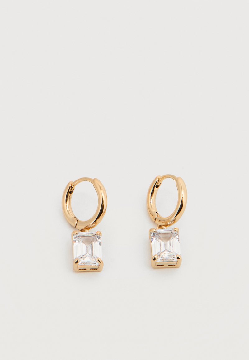 Χρυσά σκουλαρίκια κρίκοι, το καθένα με ένα κρεμαστό ορθογώνιο διαφανές λίθο στερεωμένο σε τέσσερις δαγκάνες σε λευκό φόντο.