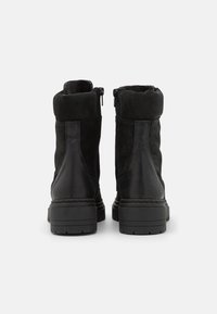 Botas pretas até ao tornozelo com parte superior em camurça, sola em borracha e fecho em zip. Ponta arredondada e destaque no calcanhar texturizado. Forro suave visível na parte superior.