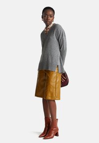 Šedý pletený svetr s žebrovými detaily, žlutá kožená sukně po kolena a hnědé boty na podpatku. Doplňky zahrnují vínovou kabelku.