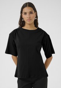 T-shirt noir en tissu jersey, avec des manches courtes à détail froncé et une coupe décontractée, et un col rond.