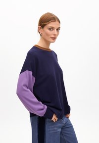 Sweter w granatowym kolorze z fioletowymi rękawami i brązowym prążkowanym kołnierzem. Luźny krój z mankietami i gładką teksturą.