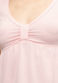 Κοντινό πλάνο ενός ατόμου που φοράει ανοιχτό ροζ τοπ με V-λαιμόκοψη και πτυχωτή λεπτομέρεια από ύφασμα στο κέντρο μπροστά.