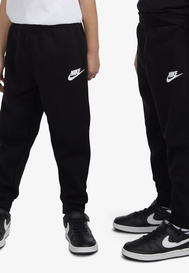 Čierne tepláky s elastickým pásom a bielym logom Nike, kombinované s čiernymi a bielymi teniskami Nike. Mäkká tkanina, voľný strih.
