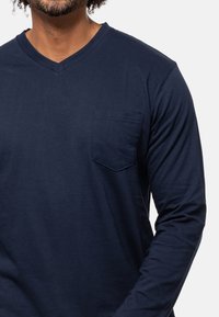 Marineblaues Langarm-T-Shirt aus Baumwolle mit V-Ausschnitt und einer linken Brusttasche. Weicher Stoff mit minimalen Nähdetails.