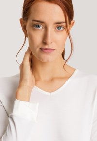 Top blanco de manga larga con escote en V y puños de satén en contraste. Tejido suave y liso con un diseño minimalista y sin patrones ni adornos visibles.