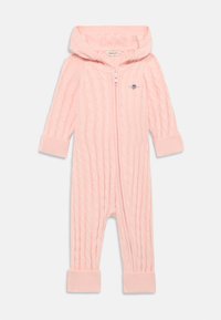 Rosa strikket overall med et teksturert kabelmønster, hette, full glidelås og ribbestrikkede mansjetter. Har et lite brodert logo på brystet.