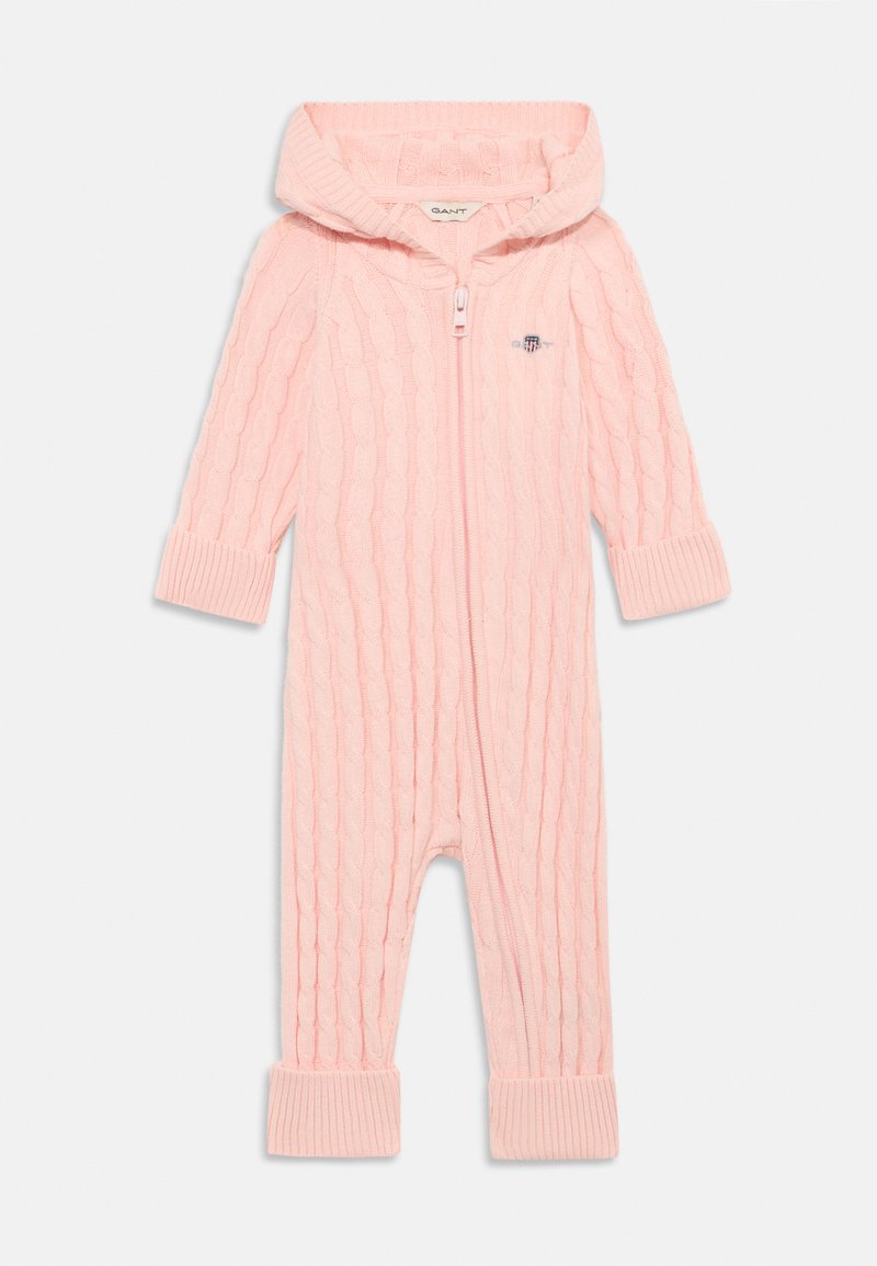 Rosa strikket overall med et teksturert kabelmønster, hette, full glidelås og ribbestrikkede mansjetter. Har et lite brodert logo på brystet.