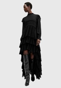 Zwarte ruches lange mouwen jurk met hoge hals, gelaagd ontwerp en asymmetrische zoom. Combinatie met zwart laarzen tot de knie.