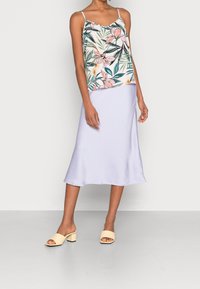 Débardeur à imprimé floral avec bretelles fines, associé à une jupe midi en satin violet clair. Modèle portant des sandales à talon bloc ouvertes beiges.