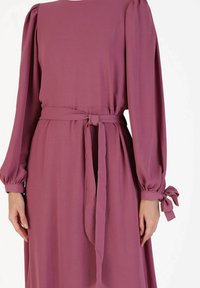 Long-sleeve, mauve dress made of soft fabric, featuring a belted waist, puffed sleeves, and tie accents at the cuffs.