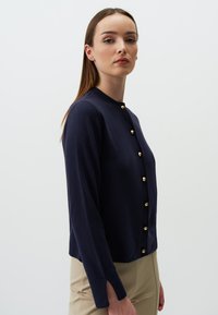 Navy-blauer Langarm-Cardigan mit goldenen Knöpfen, Rundhalsauschnitt und subtiler Textur, mit Schlitzen an den Manschetten für zusätzlichen Detail.
