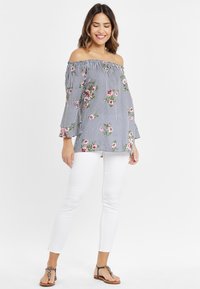 Off-shoulder blus med marinblå och vita ränder, blommönster i rosa och grönt, utsvängda ärmar, parat med vita jeans och platta sandaler.