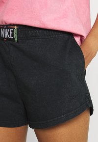 Juodi sportiniai šortai su grioveliu, pasižymintys spalvingu Nike juosmeniu ir šoninėmis kišenėmis. Minimalistinis dizainas su subtiliu logotipu.