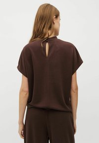 Bruine top met korte mouwen en een sleutelgatdetail aan de achterkant, gemaakt van zachte, gladde stof, met een oversized pasvorm en ronde halslijn.