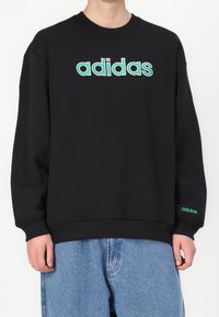 Svart sweatshirt i bomullsblandning, med en stor turkos "adidas"-logotyp på framsidan och en mindre logotyp på ärmen.