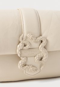 Cream leather clutch with a textured snake-shaped clasp and an engraved logo plate. Features a smooth finish and a fold-over design.