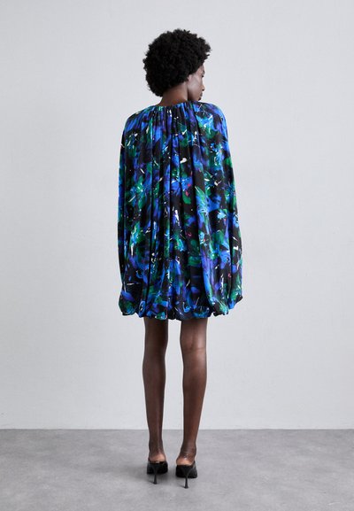 Robe florale noire et bleue avec des manches flottantes et amples et un ourlet élastique. Tissu lisse avec une finition brillante. Portée avec des chaussures à talons hauts.