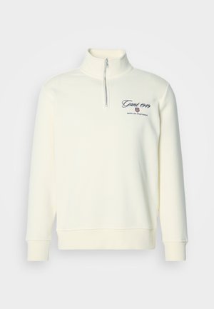 Sweatshirt într-o nuanță off-white, cu fermoar până la jumătate, având brodați pe pieptul stâng „Gant 1949” și logo-ul de îmbrăcăminte sportivă americană. Manșetele și tivul sunt culisați.