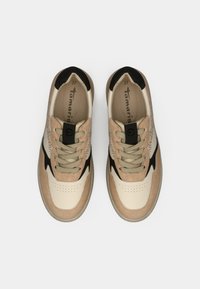 Μπεζ και μαύρα αθλητικά παπούτσια με υφή στο πάνω μέρος, κοπές αερισμού και καφέ λεπτομέρειες. Διαθέτουν στρογγυλά κορδόνια και μαλακή σόλα.